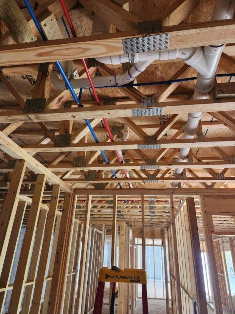 Framed interior of a house showing plumbing, electrical wiring, and a ladder.